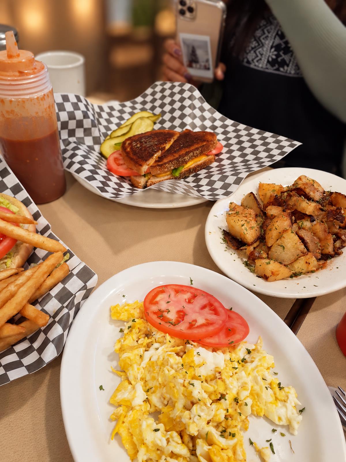 Breakfast table with eggs, home fries, toast and a grilled sandwich